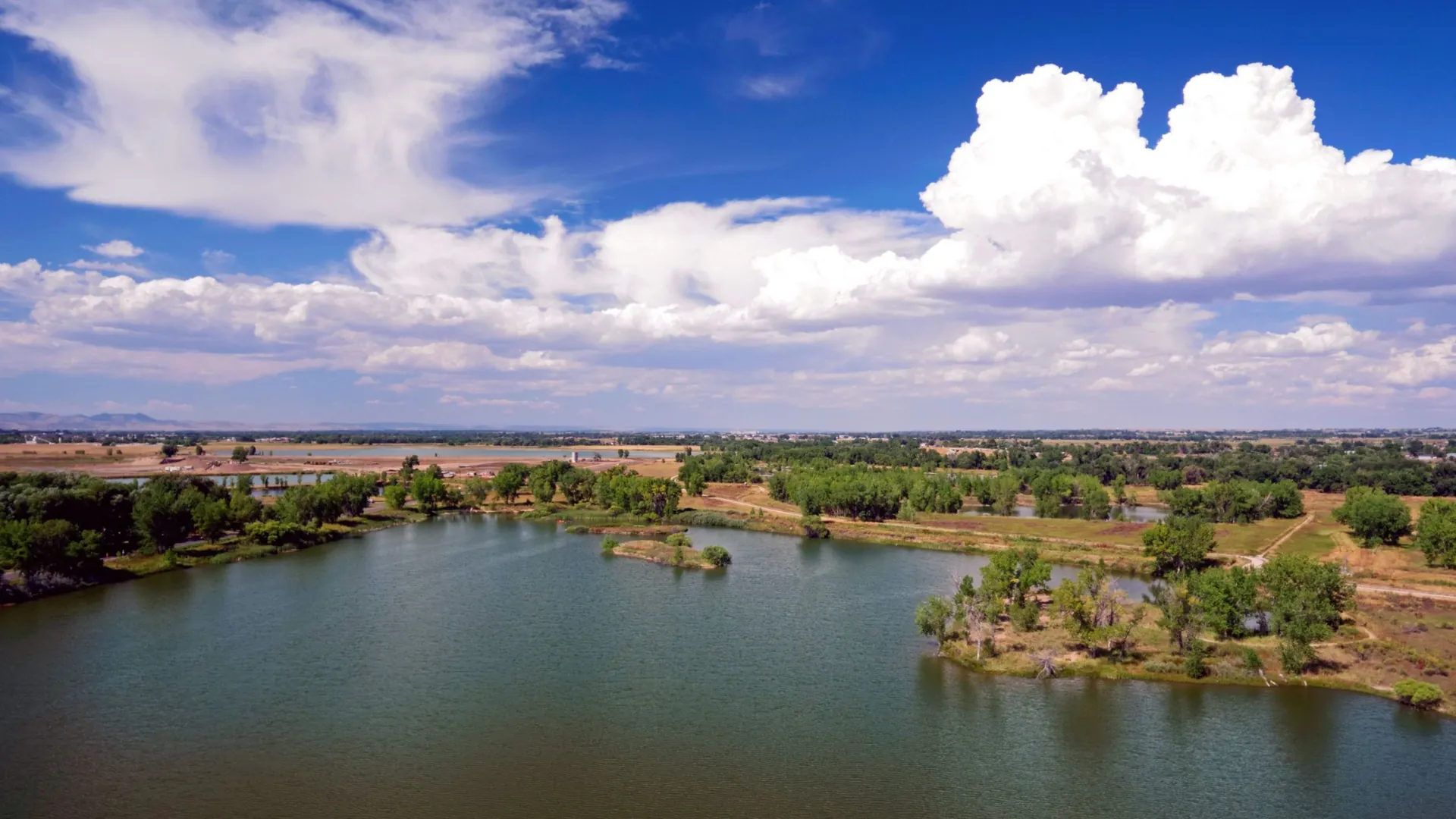 A Northern Colorado reservoir ringed by cottonwoods, with farmland beyond and low mountains on the horizon